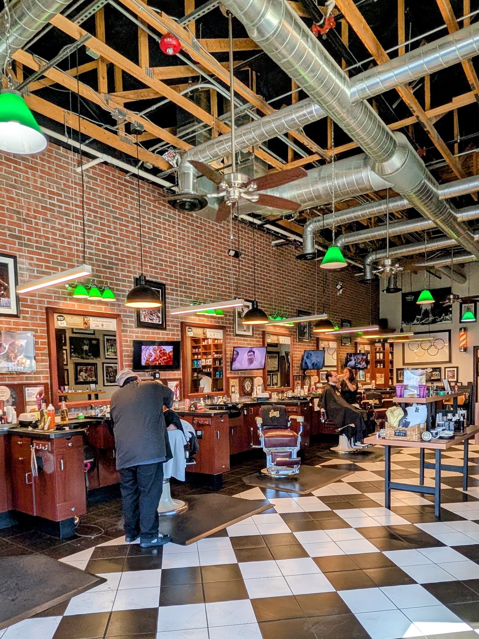 Spacious barbershop interior with exposed beams, brick walls, barber stations and a checkered floor