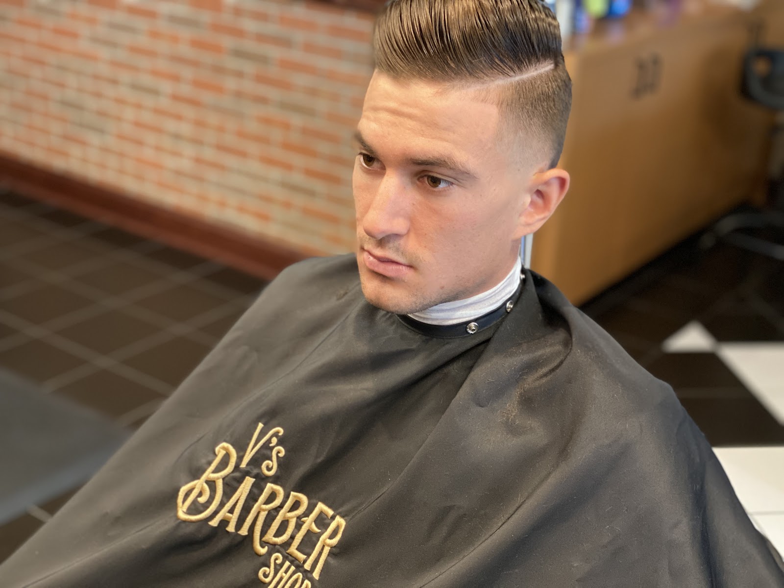 Close-up of a man with a sharp pompadour fade haircut wearing a V's Barber Shop cape