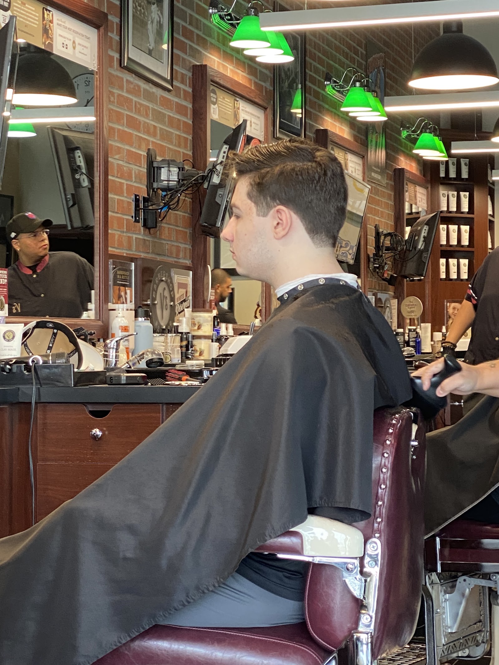 Client in a barber chair with a fresh cut, barbers and brick interior in the background