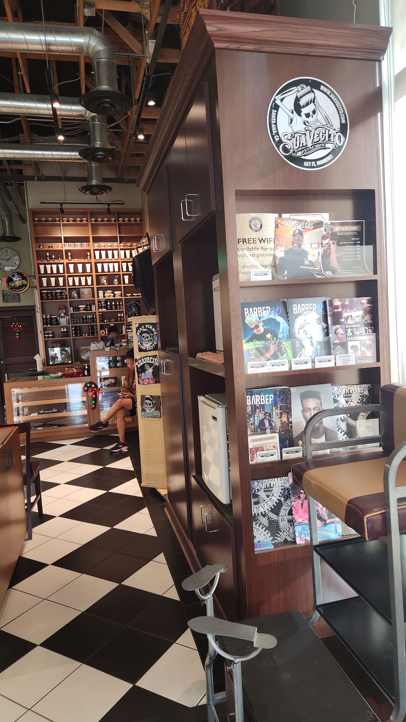 Barbershop interior showing a product wall and a magazine rack with the Suavecito logo over a checkered floor