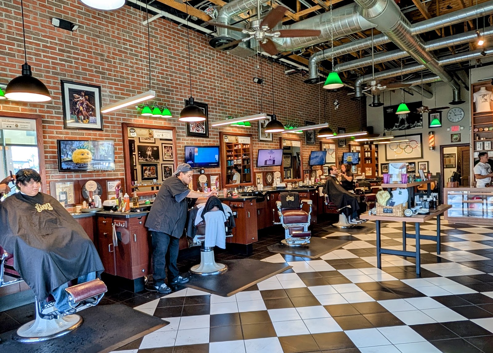 Interior of V's Barbershop with barbers cutting hair, brick walls, green pendant lights and a checkered floor